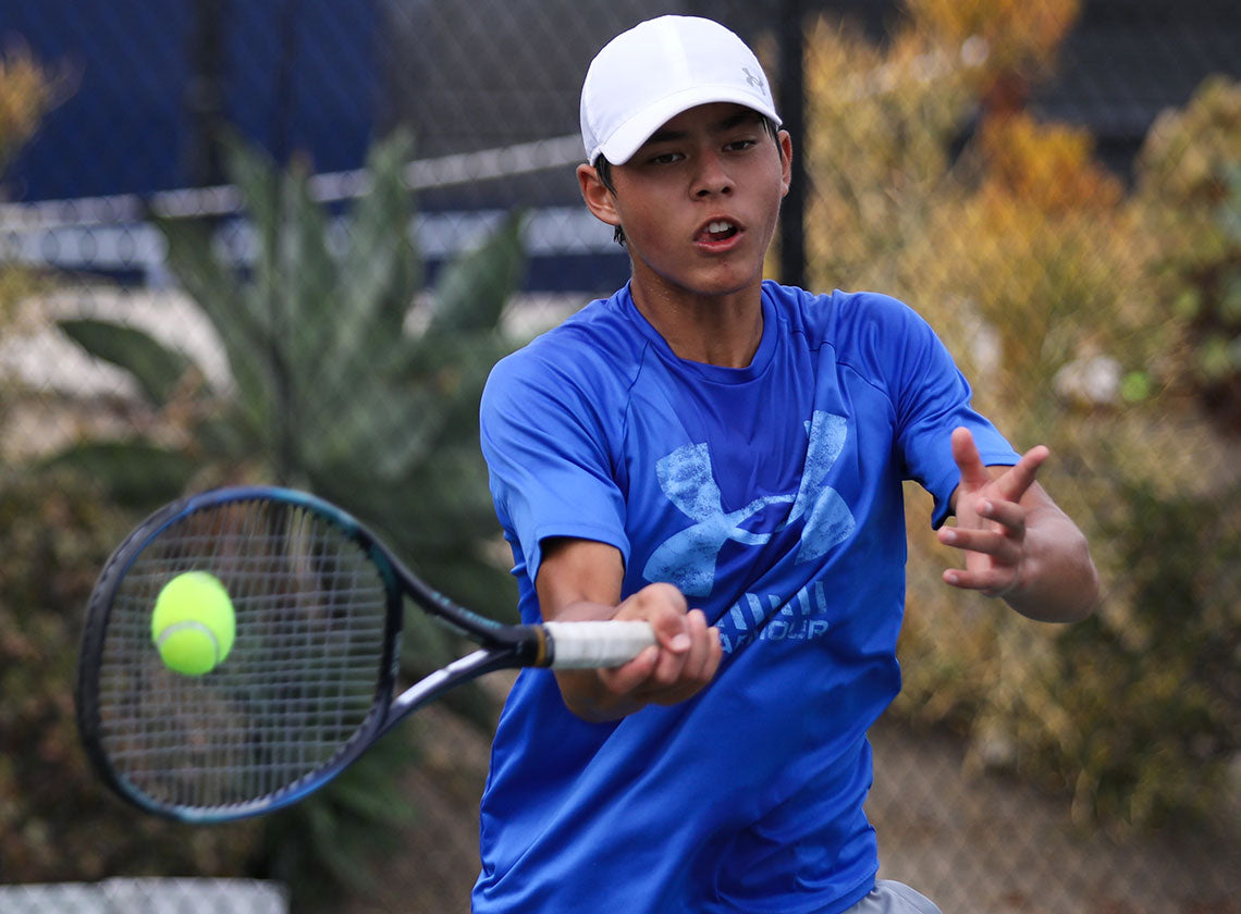Boy, wearing white hat and blue shirt, hits a forehand at UTR Sports junior tennis tournaments