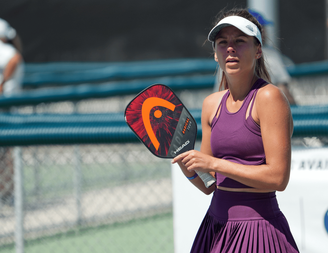 Woman wearing purple dress plays pickleball with a paddle in her hand with Universal Tennis